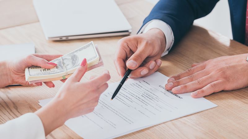 partial view of businessman pointing at signature place in loan agreement near client holding money